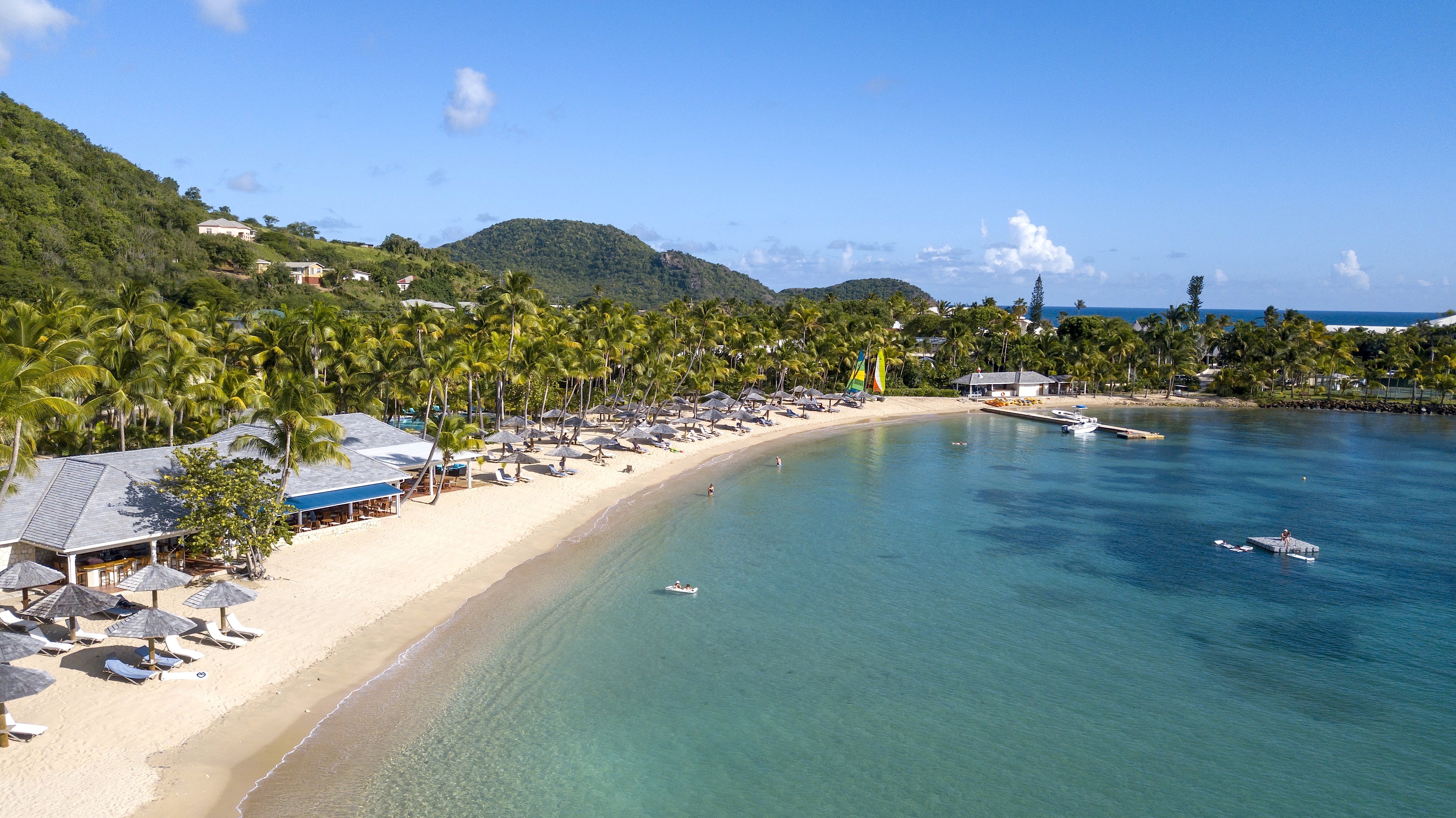 Turquois sea and white sand beach with hills and palms beyond