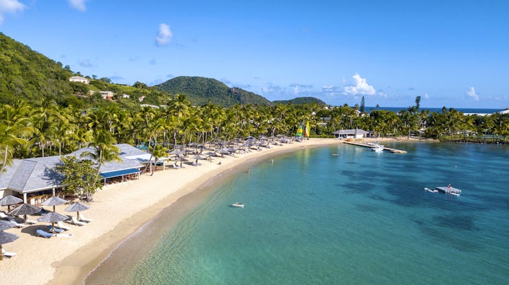 Turquois sea and white sand beach with hills and palms beyond