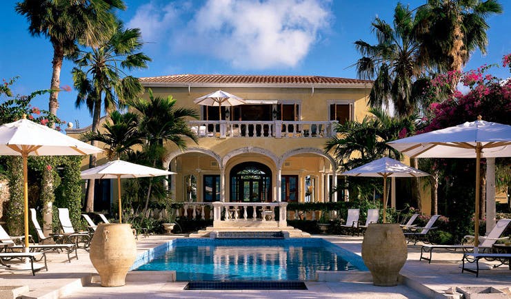 Jumby Bay Antigua pool sun loungers umbrellas hotel building in background