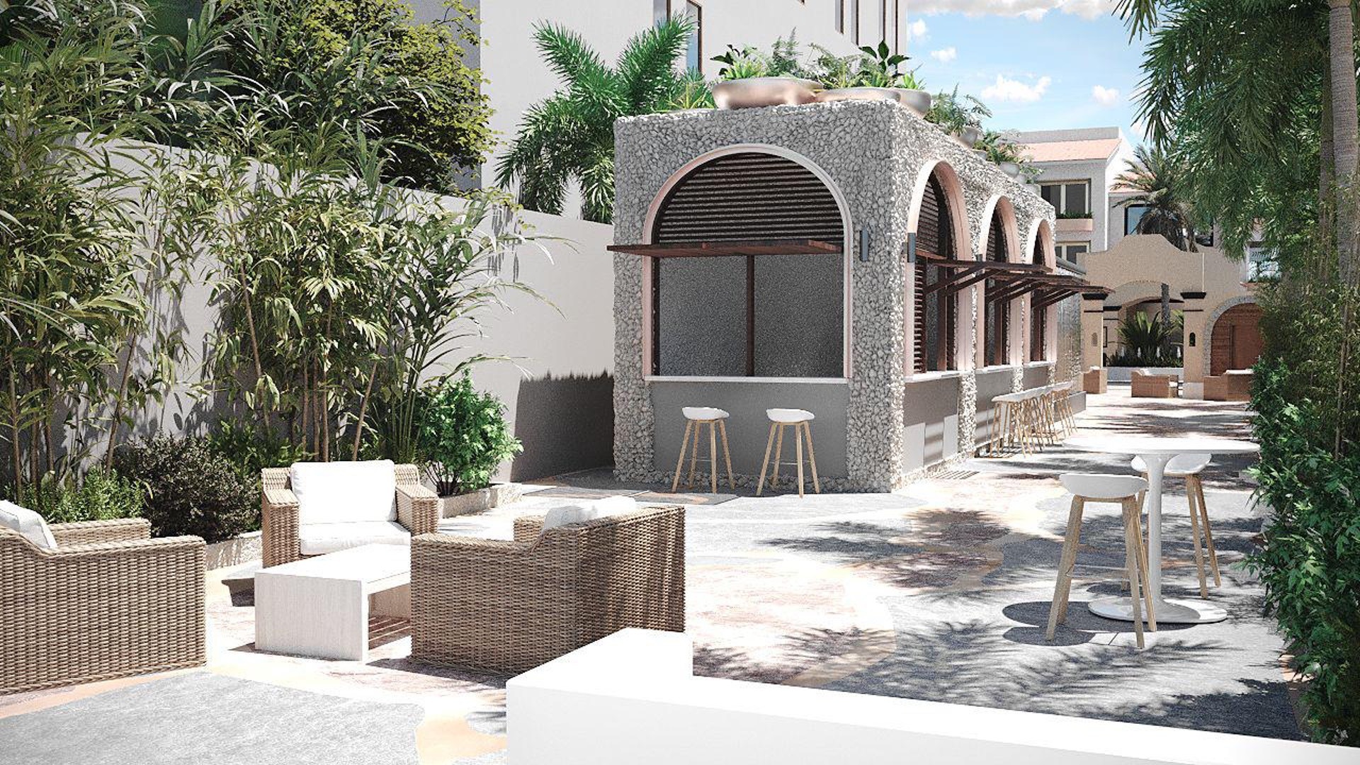 Blue Monkey Hotel beach club outdoor seating, with some white stools gathered at glass tables and some comfortable sofas around a coffee table, with trees and shrubs behind