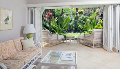 Living room area in a garden view suite with sofa in the room and doors opening onto the garden with sun loungers