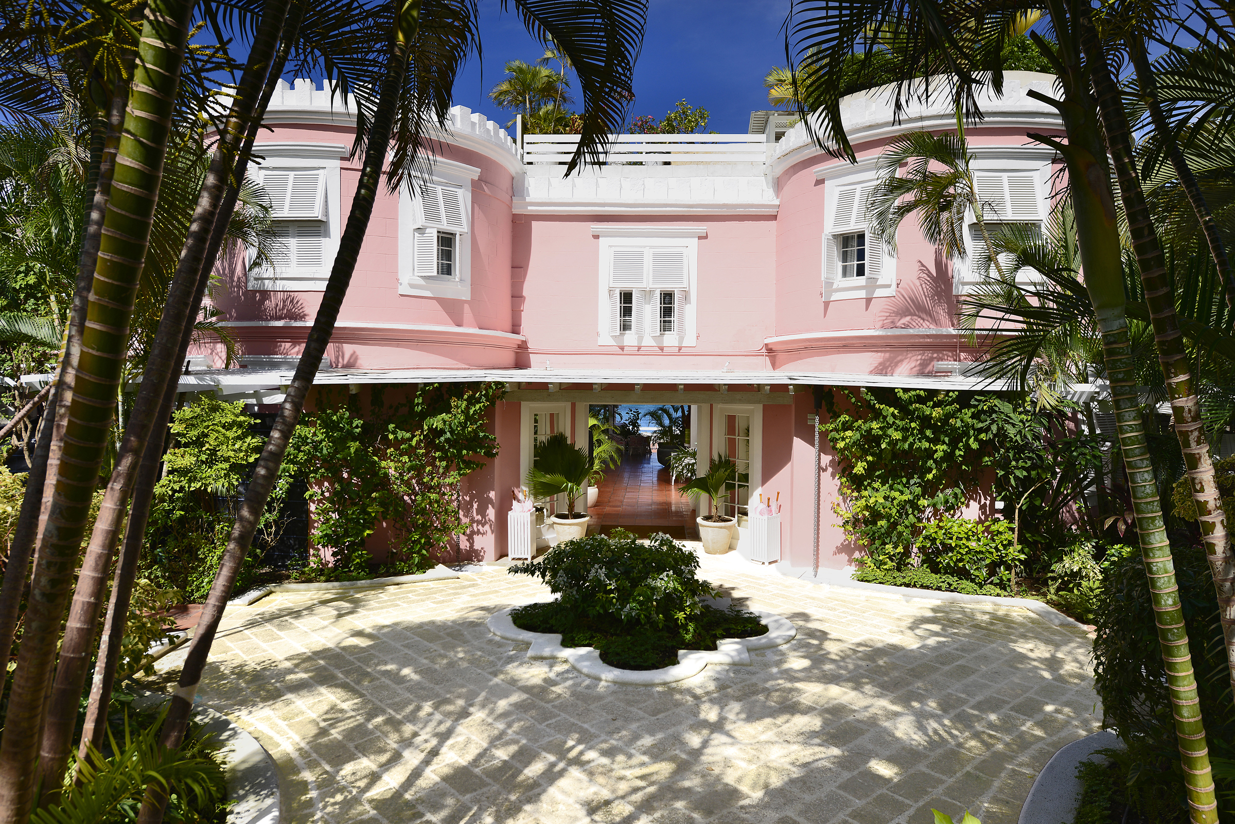 Great House with pink exterior building, white shutters covering the windows and palm trees around