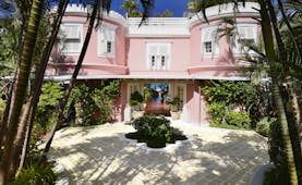 Great House with pink exterior building, white shutters covering the windows and palm trees around