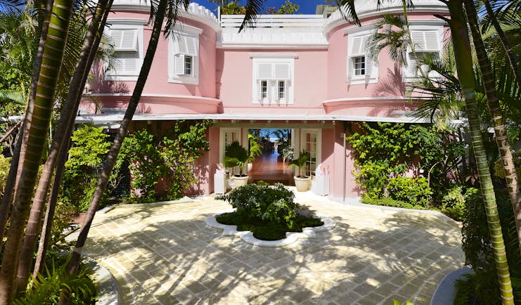 Great House with pink exterior building, white shutters covering the windows and palm trees around