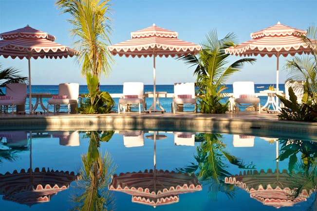 Outdoor pool with pink umbrellas and sunloungers around the edge of the pool reflecting in the pool