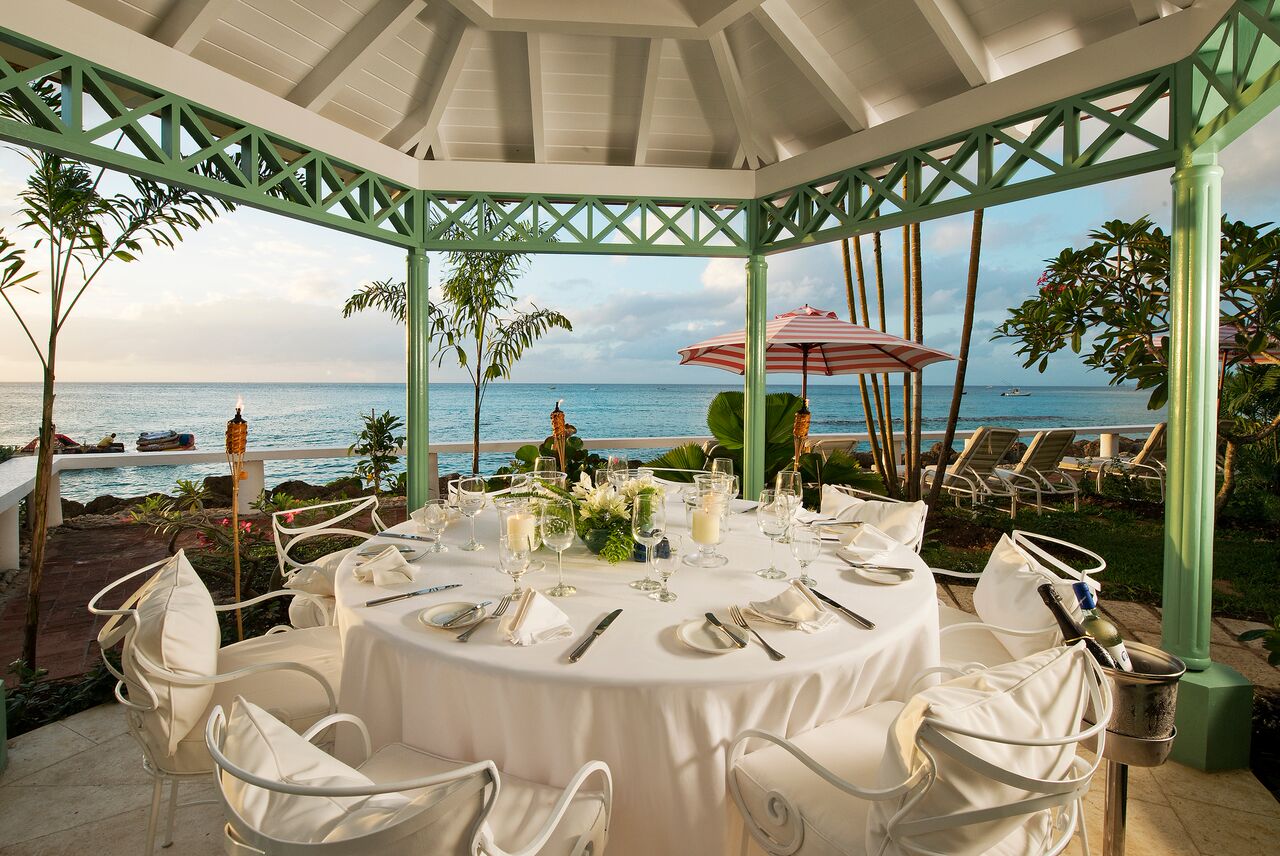 Pavilion with table set up for dining underneath and view of sea in distance