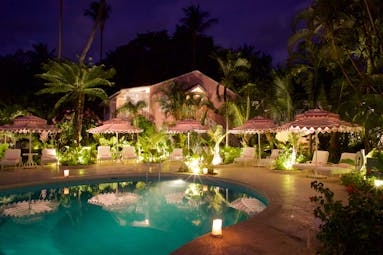 Pool at night with pink hotel exterior building in background, pink and white umbrellas and pool lights 