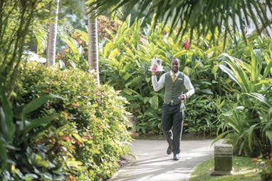 Coral Reef Club Barbados smiling waiter carrying tray and drinks across the gardens