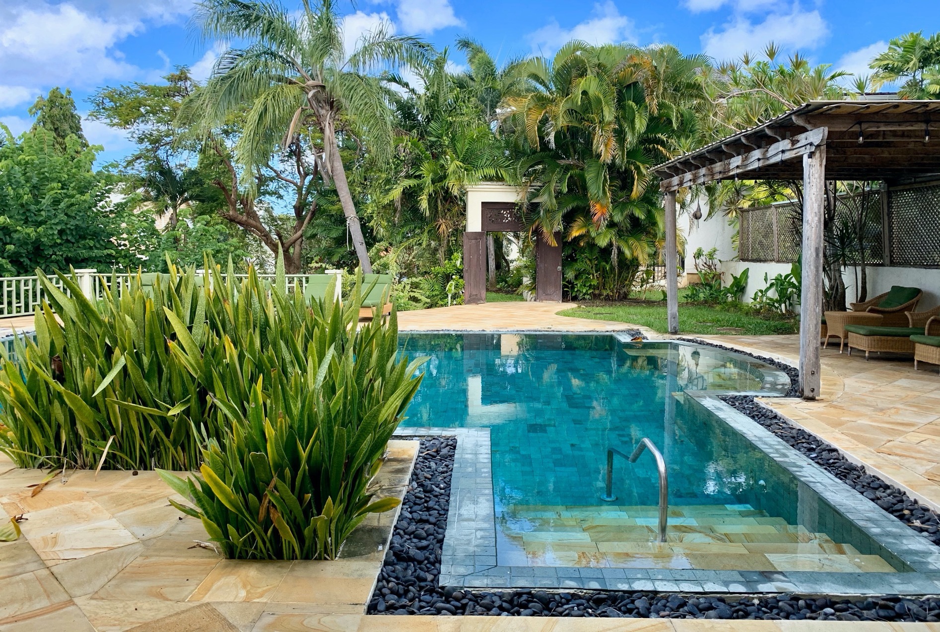 Little Good Harbour swimming pool with turquoise water, lined with marbled grey and brown tiles, and surrounded by palm trees and shrubs