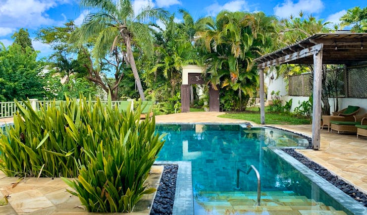 Little Good Harbour swimming pool with turquoise water, lined with marbled grey and brown tiles, and surrounded by palm trees and shrubs