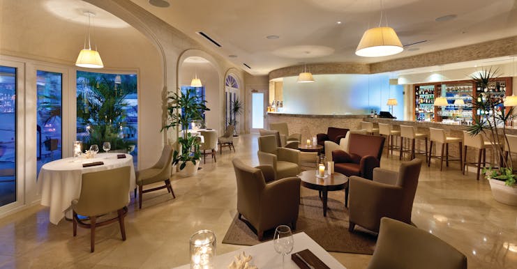 Bar at the Port Ferdinand with a bar stools sat behind the bar with a drinks cabinet. Seating areas are scattered around the room 