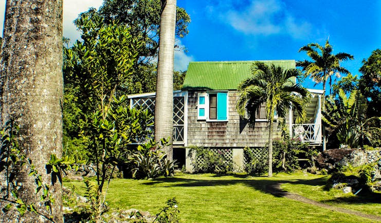 Palm trees and grass with small cottasge with green roof and blue shtters at Hermitage Inn Nevis