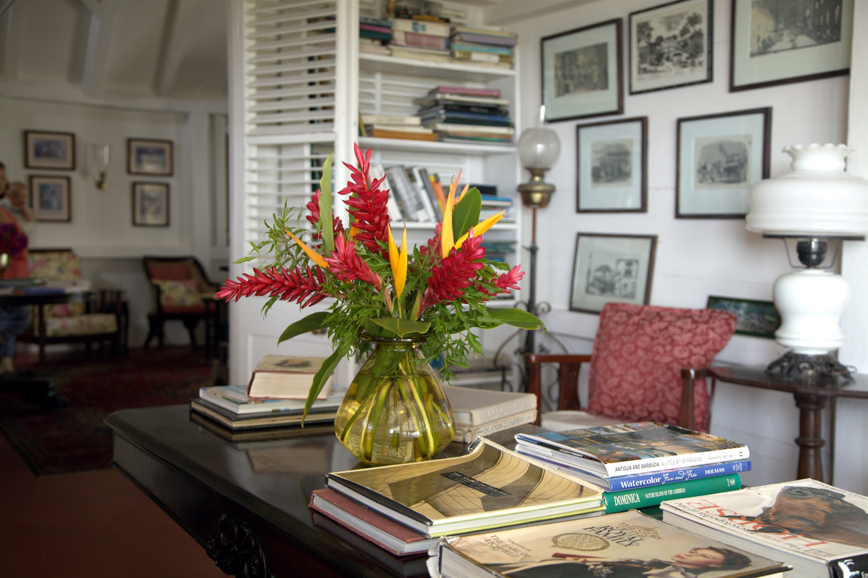 Red and yellow heliconia in vase on desk in lounge with books and framed pictures at Hermitage Inn Nevis