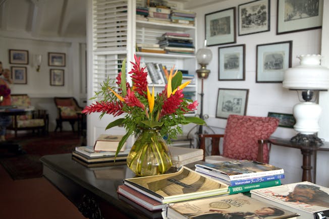 Red and yellow heliconia in vase on desk in lounge with books and framed pictures at Hermitage Inn Nevis