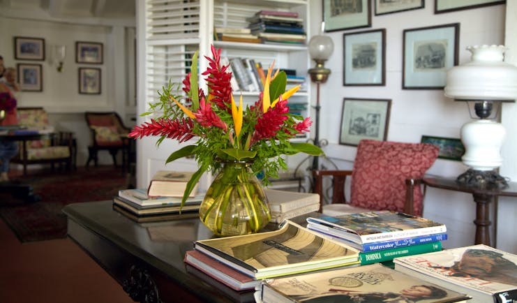 Red and yellow heliconia in vase on desk in lounge with books and framed pictures at Hermitage Inn Nevis