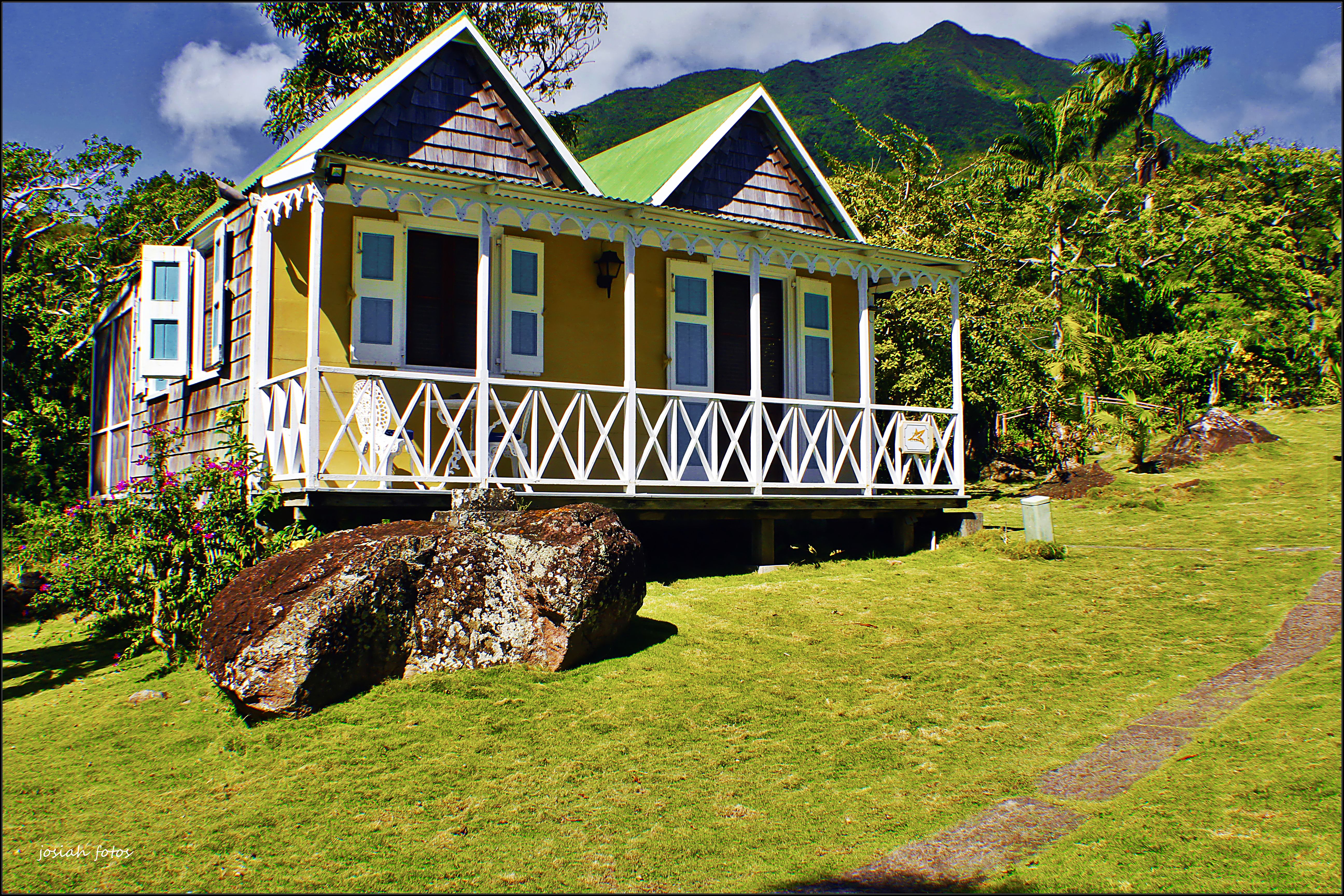 Yellow cottage with white verandah on grassy slope at Hermitage Inn Nevis