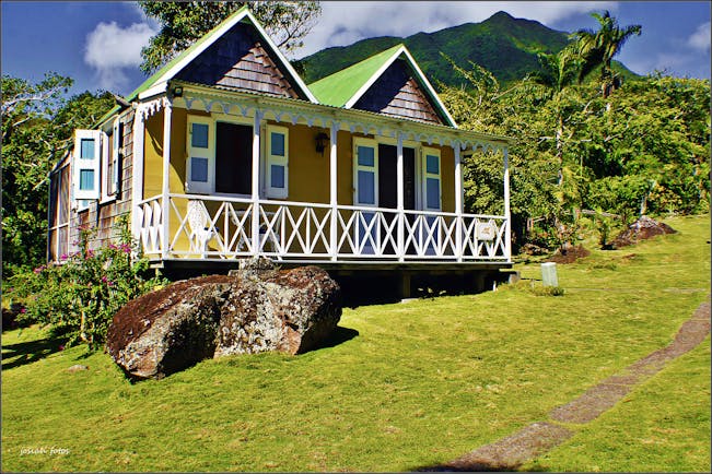 Yellow cottage with white verandah on grassy slope at Hermitage Inn Nevis