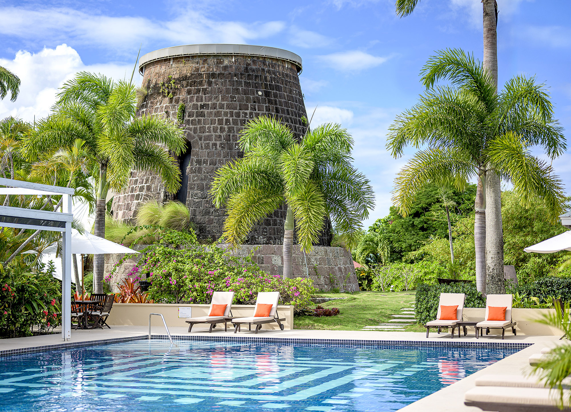 Montpelier Nevis swimming pool with blue water, sun loungers, grass and palm trees, and a turret building behind