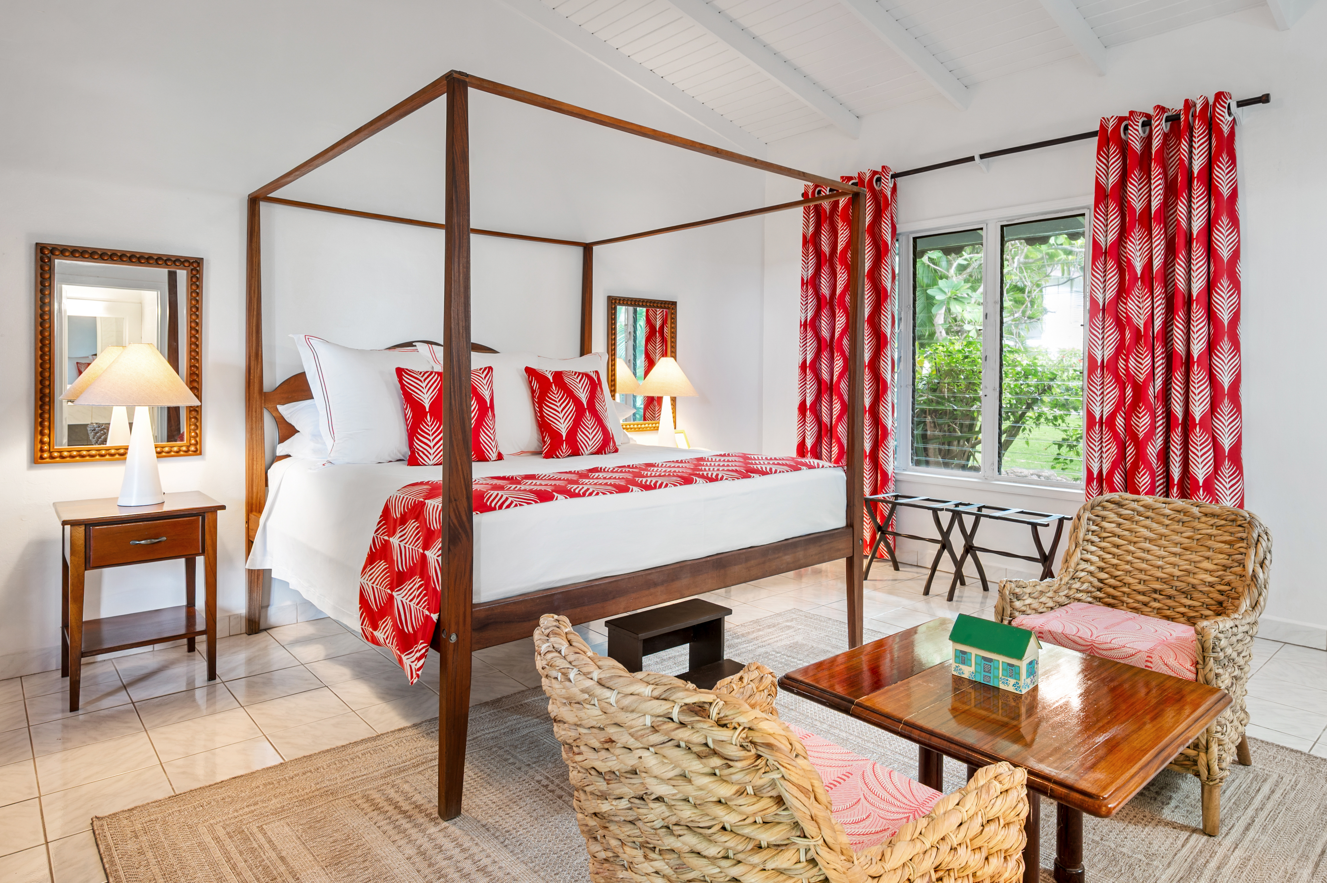 Montpelier Nevis Premier Room with tiled floor, wooden four-poster bed, white walls, and burst of pink