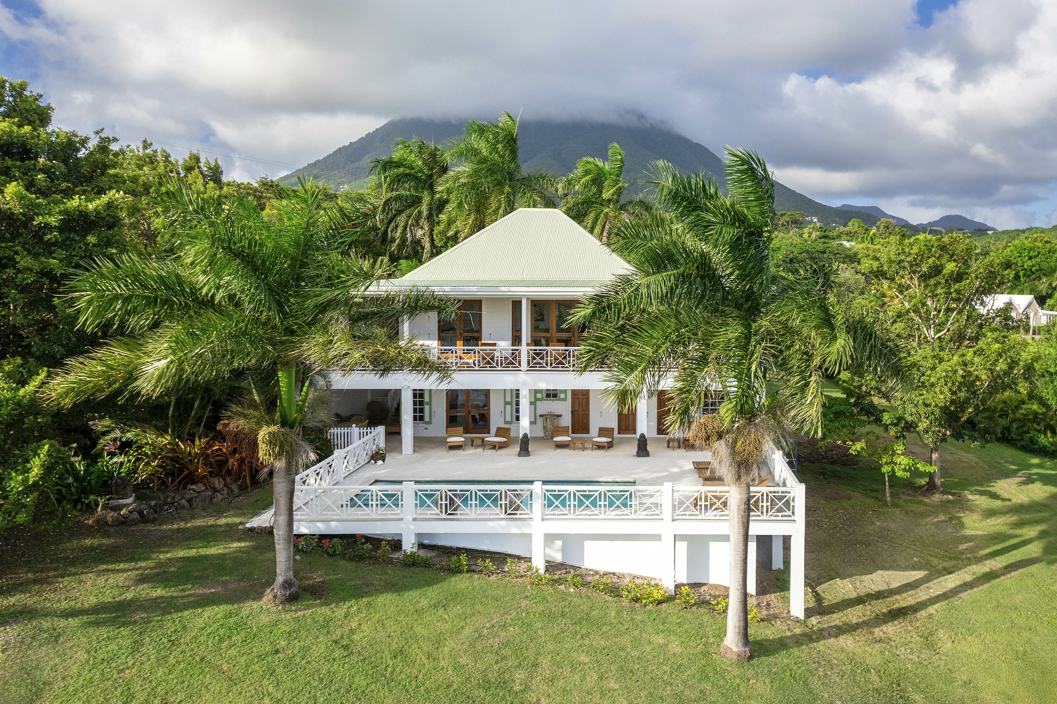 Montpelier Nevis villa set against jungle and mountain scenery, with raise pool terrace and two-storey building in white wood