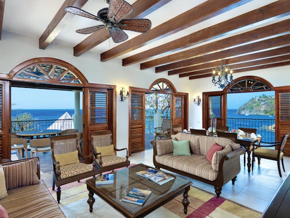 Cap Maison St Lucia suite lounge indoor seating area with sofa and armchairs leading 6o balcony with ocean views
