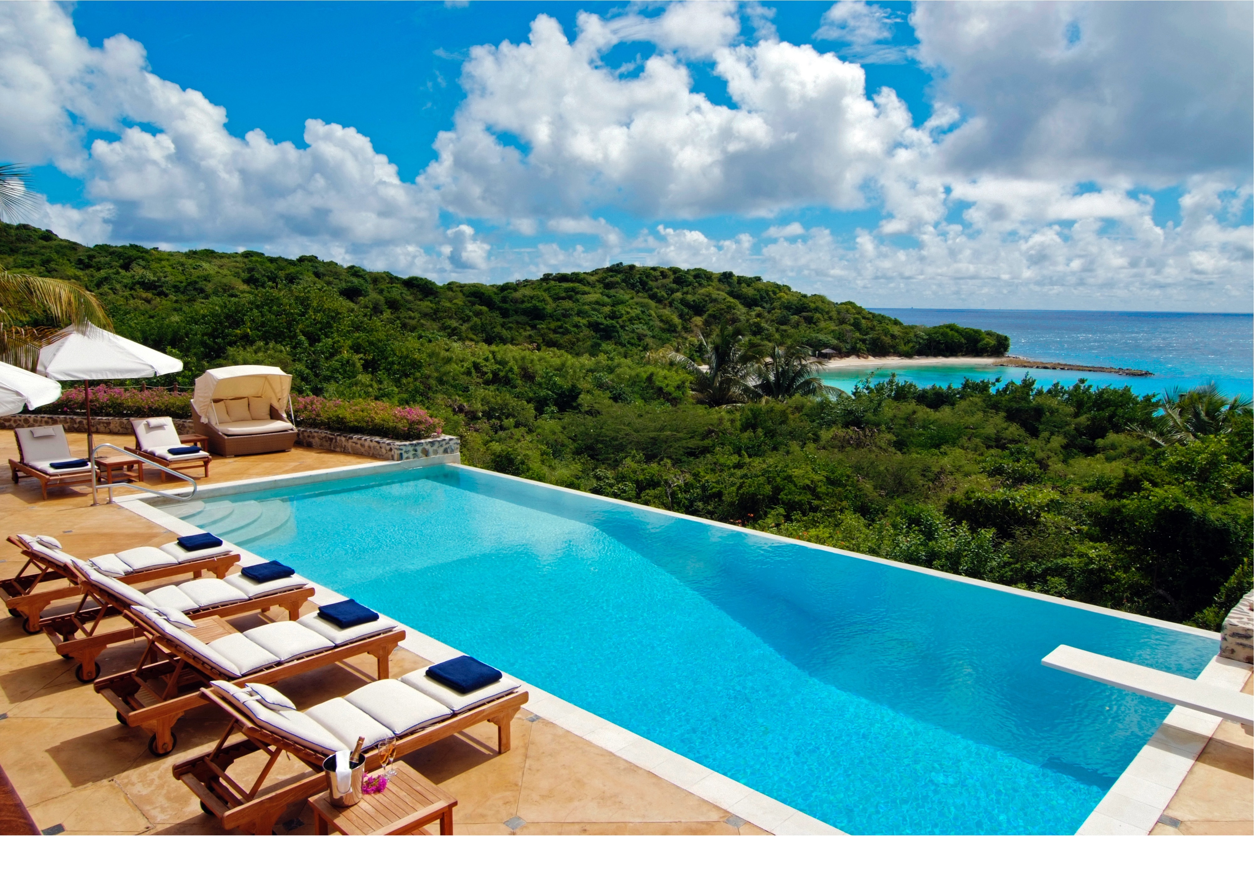Canouan Estate infinity pool looking over trees and seafront, with diving board and loungers