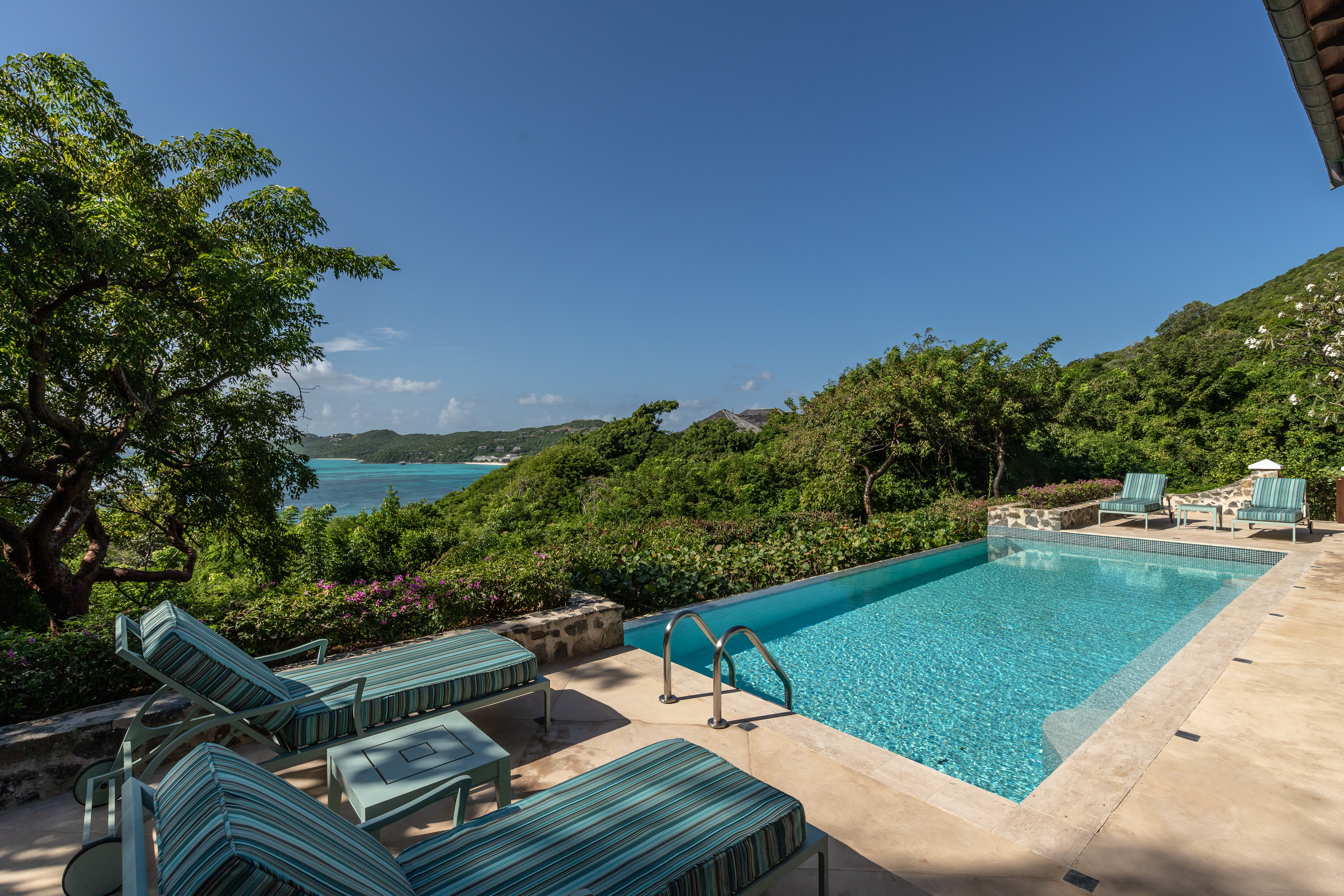 Canouan Estate villa pool, looking out over trees and sea, with blue sun loungers
