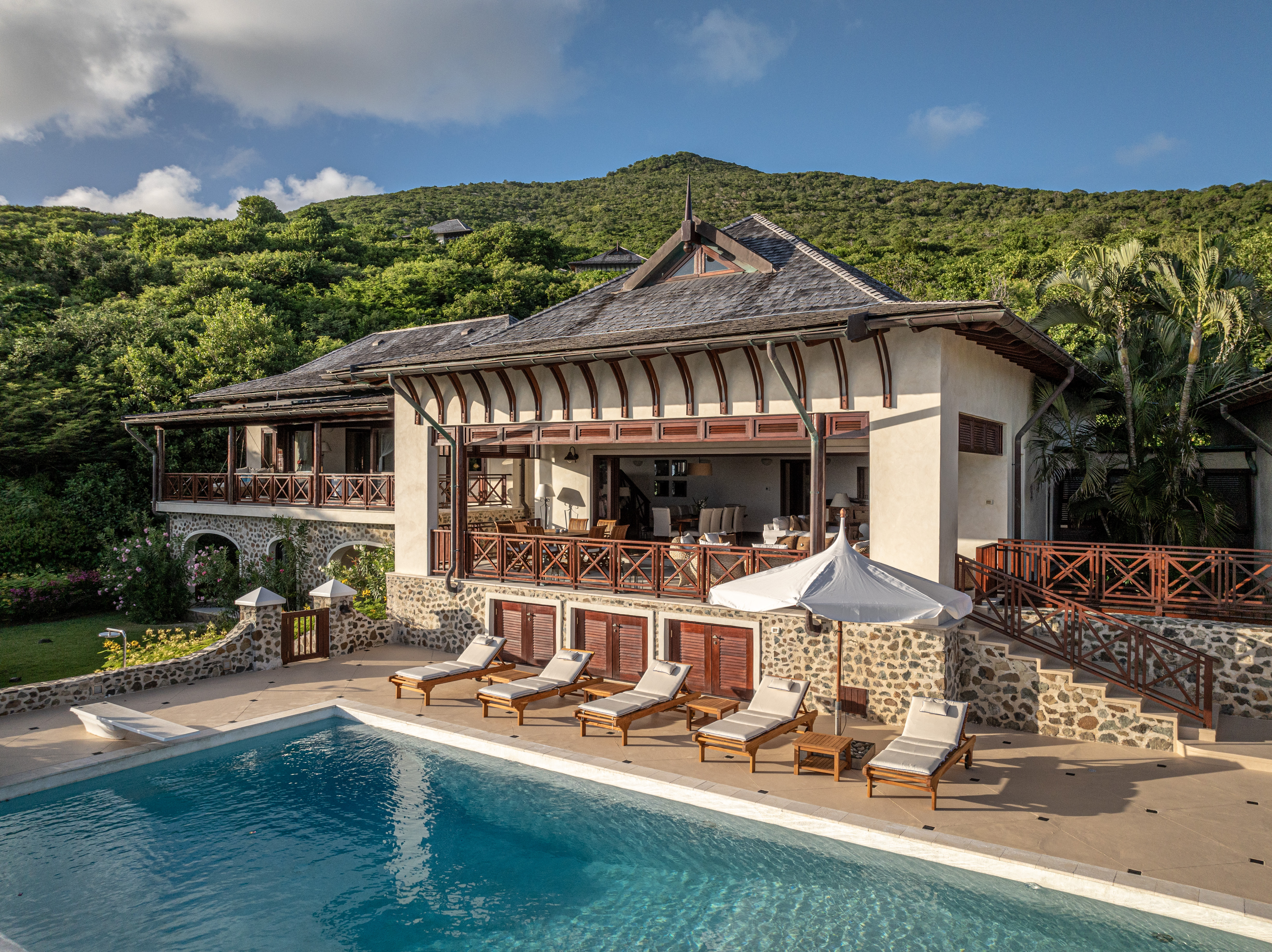 Canouan Estate Villa exterior with opening wall, sun loungers around a large pool, and rustic architecture