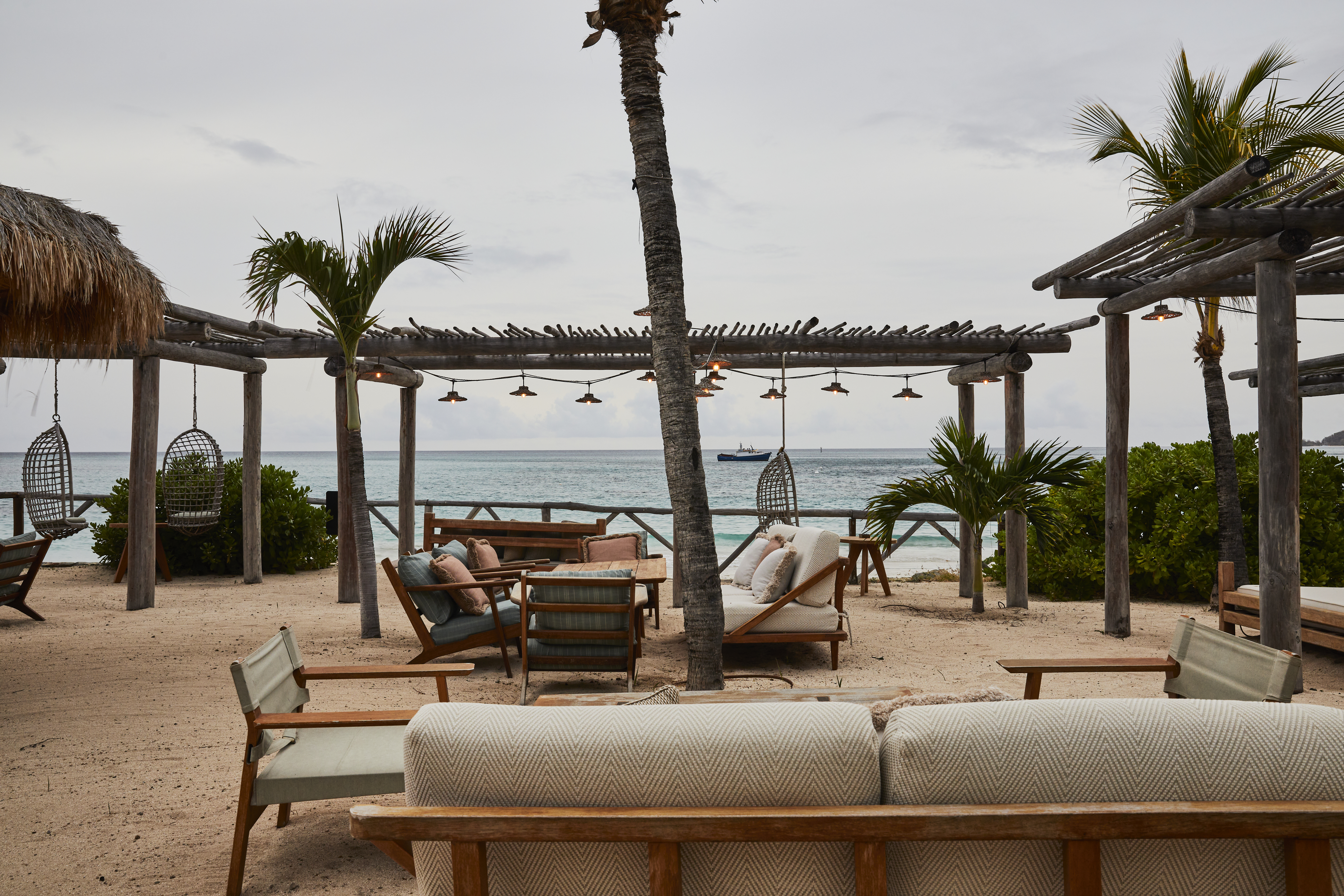 Soho Beach House Canouan beach bar with sofas, chairs, canopies, and palm trees on the sand