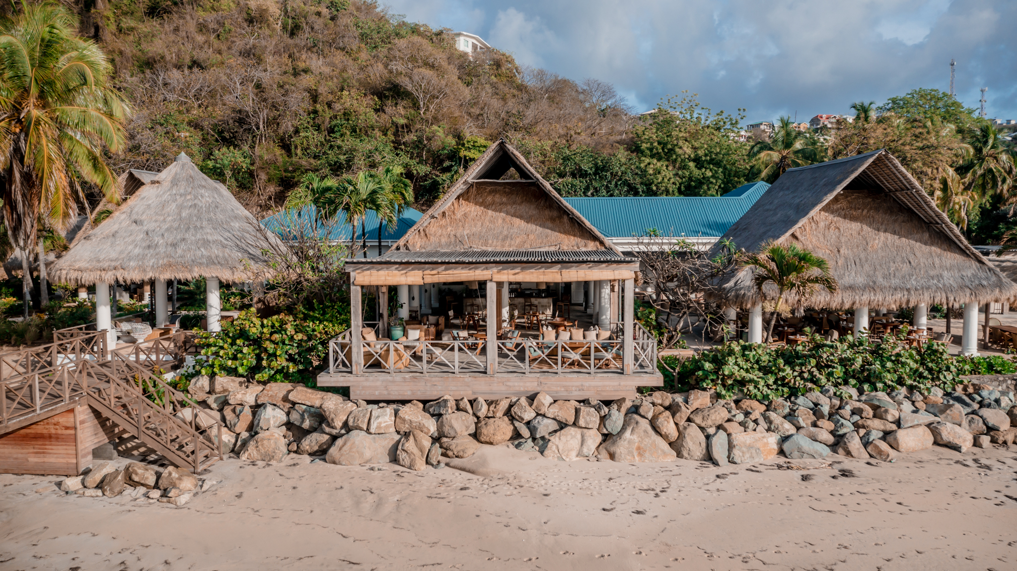 Soho Beach House Canouan exterior view showing main hotel area, with thatched roofs, terraces, and sandy beach