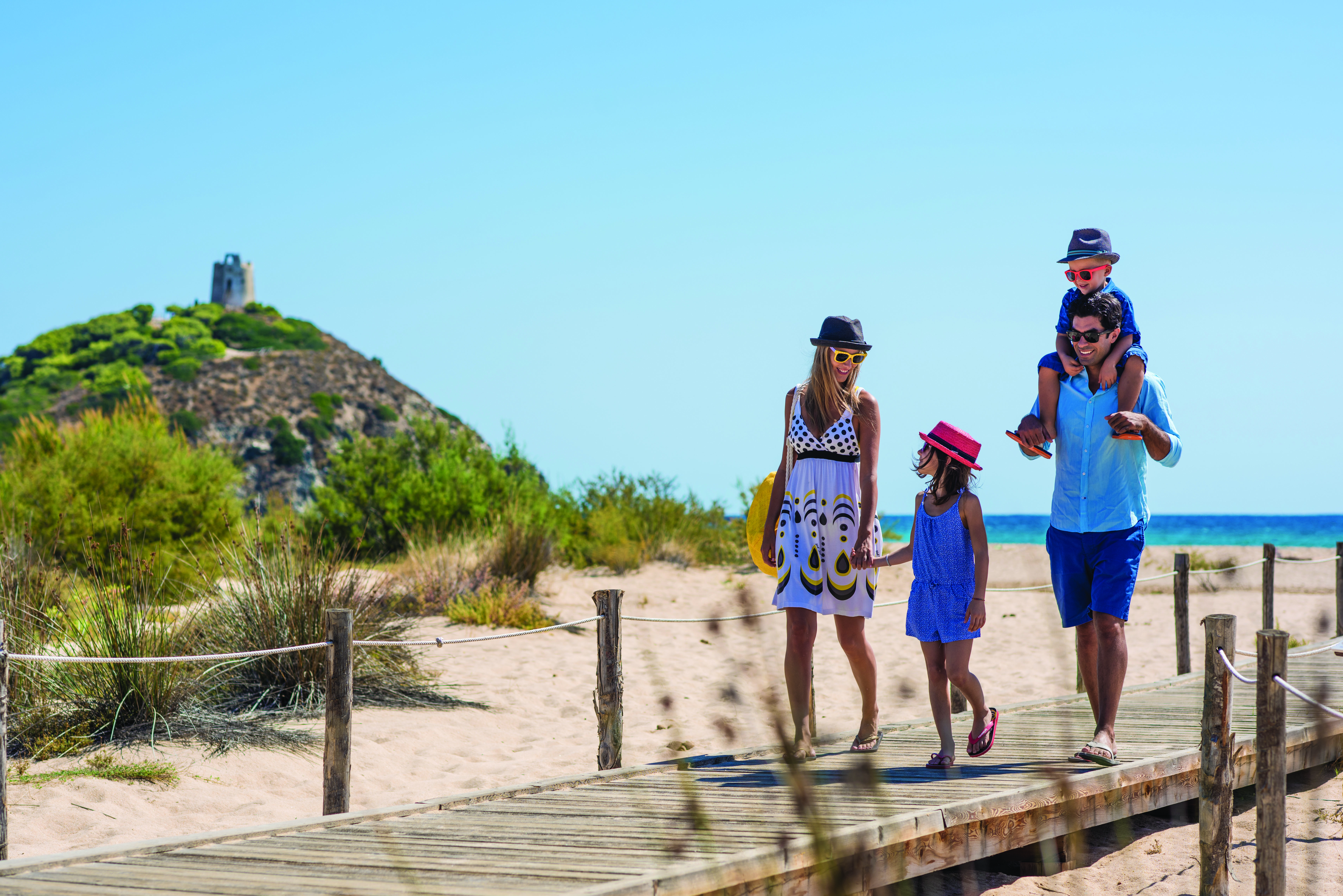 Two adults and two children walking on planks on sandy beach