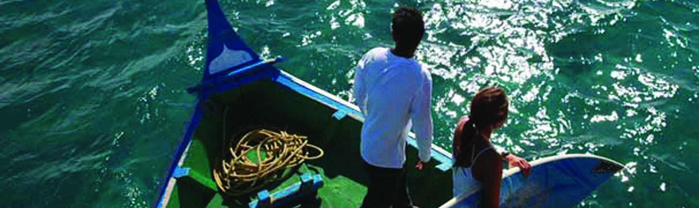 Two people on boat on calm turquose sea with one holding windsurfing board