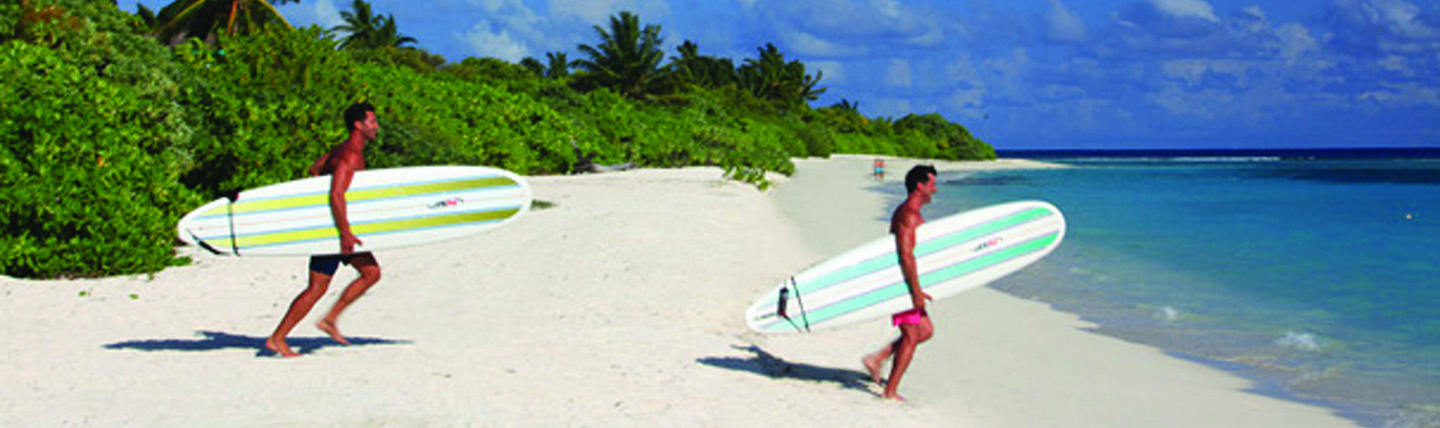 Two men on white sand beach carrying windsurfing boards into the sea