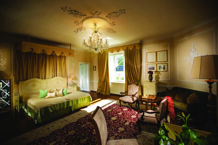 Hotel Bristol Salzburg junior suite with gold, green and red colour scheme with large double bed, sofa, armchairs and chandelier