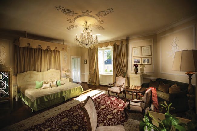 Hotel Bristol Salzburg junior suite with gold, green and red colour scheme with large double bed, sofa, armchairs and chandelier