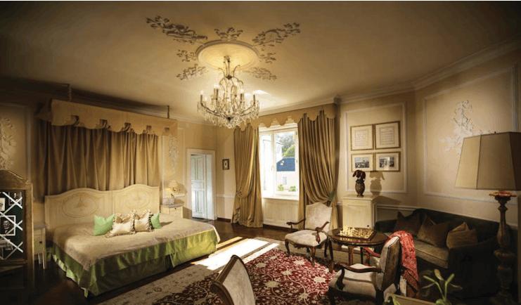 Hotel Bristol Salzburg junior suite with gold, green and red colour scheme with large double bed, sofa, armchairs and chandelier
