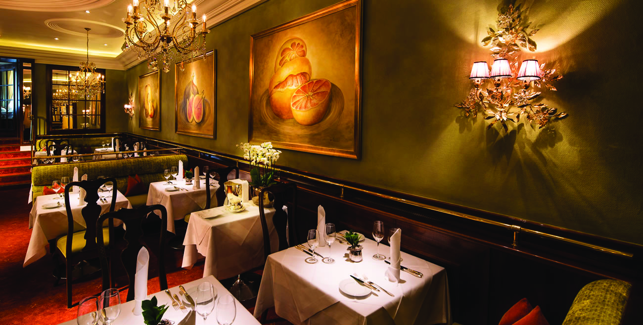 Hotel Bristol Salzburg restaurant dining area with green walls, chandeliers and dining tables set up 