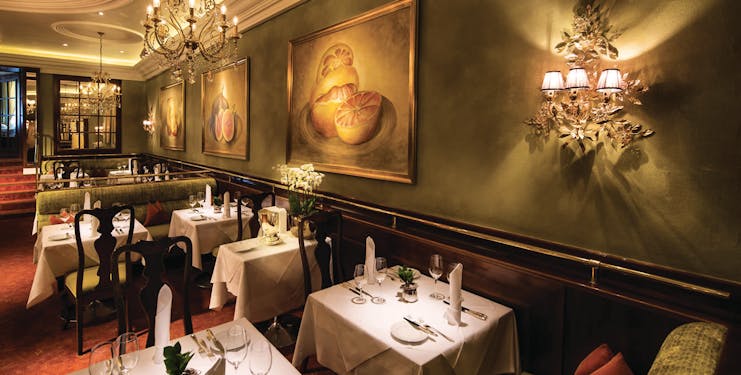 Hotel Bristol Salzburg restaurant dining area with green walls, chandeliers and dining tables set up 