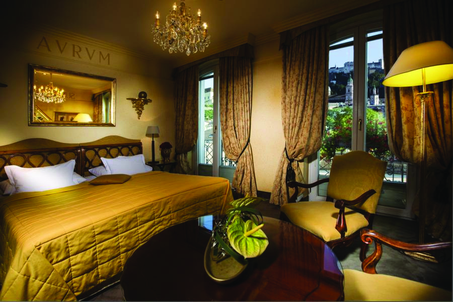 Hotel Bristol Salzburg standard room with green and beige colour scheme, large double bed, arm chairs, mirror and chandelier