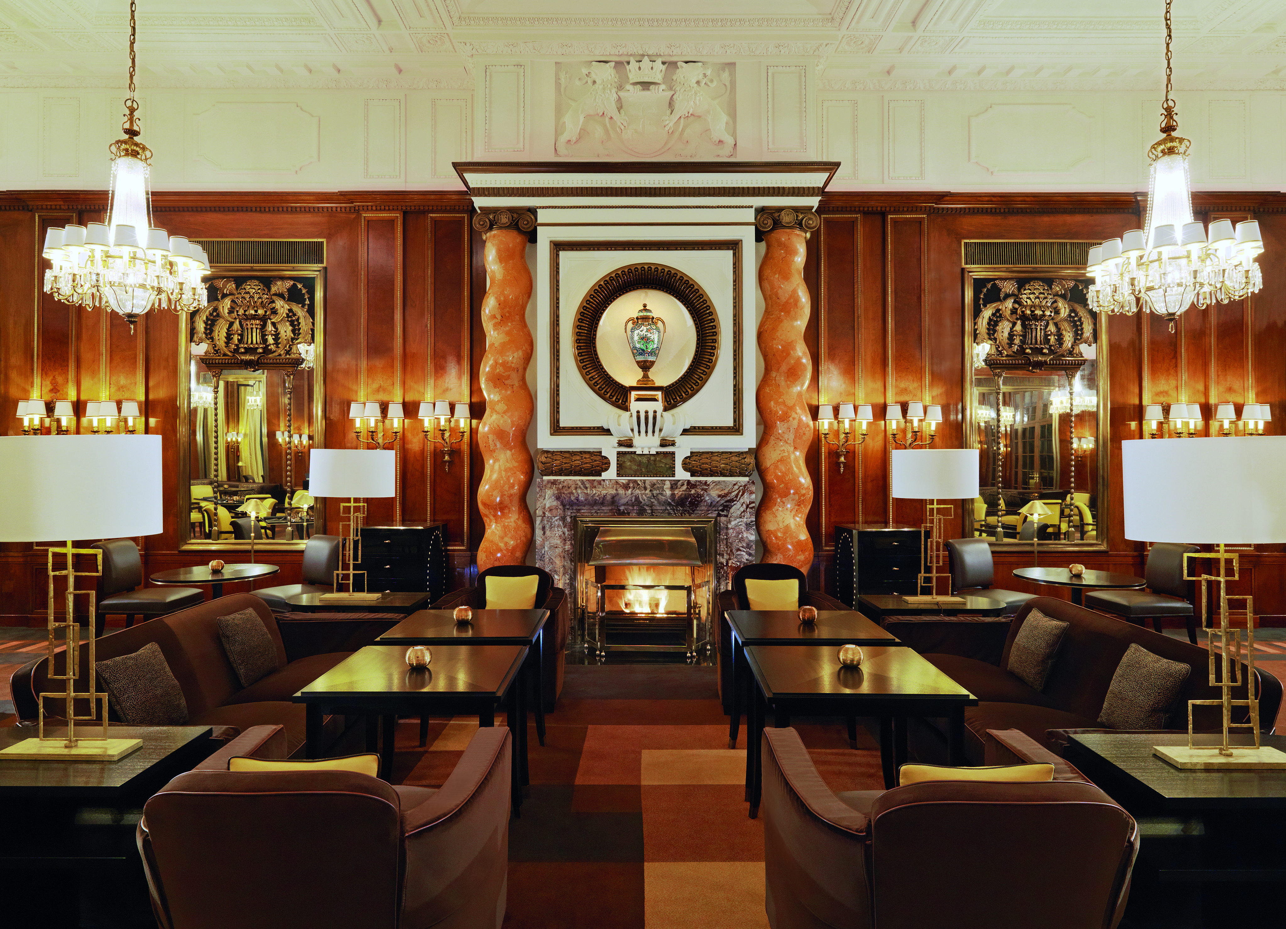 Hotel Bristol Vienna lounge area with several dark wood tables marble columns large fireplace and chandeliers