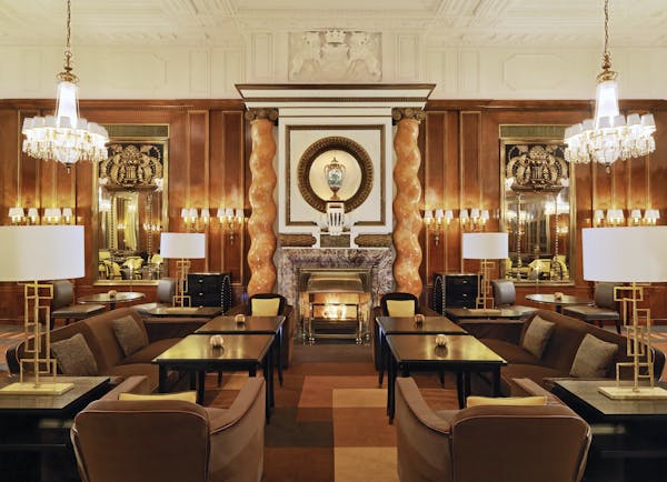 Hotel Bristol Vienna lounge area with several dark wood tables marble columns large fireplace and chandeliers