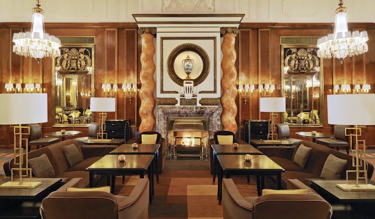 Hotel Bristol Vienna lounge area with several dark wood tables marble columns large fireplace and chandeliers