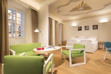 Hotel Goldgasse double bed on one side of a large spacious modern stylised room with a wooden floor and seating around a table