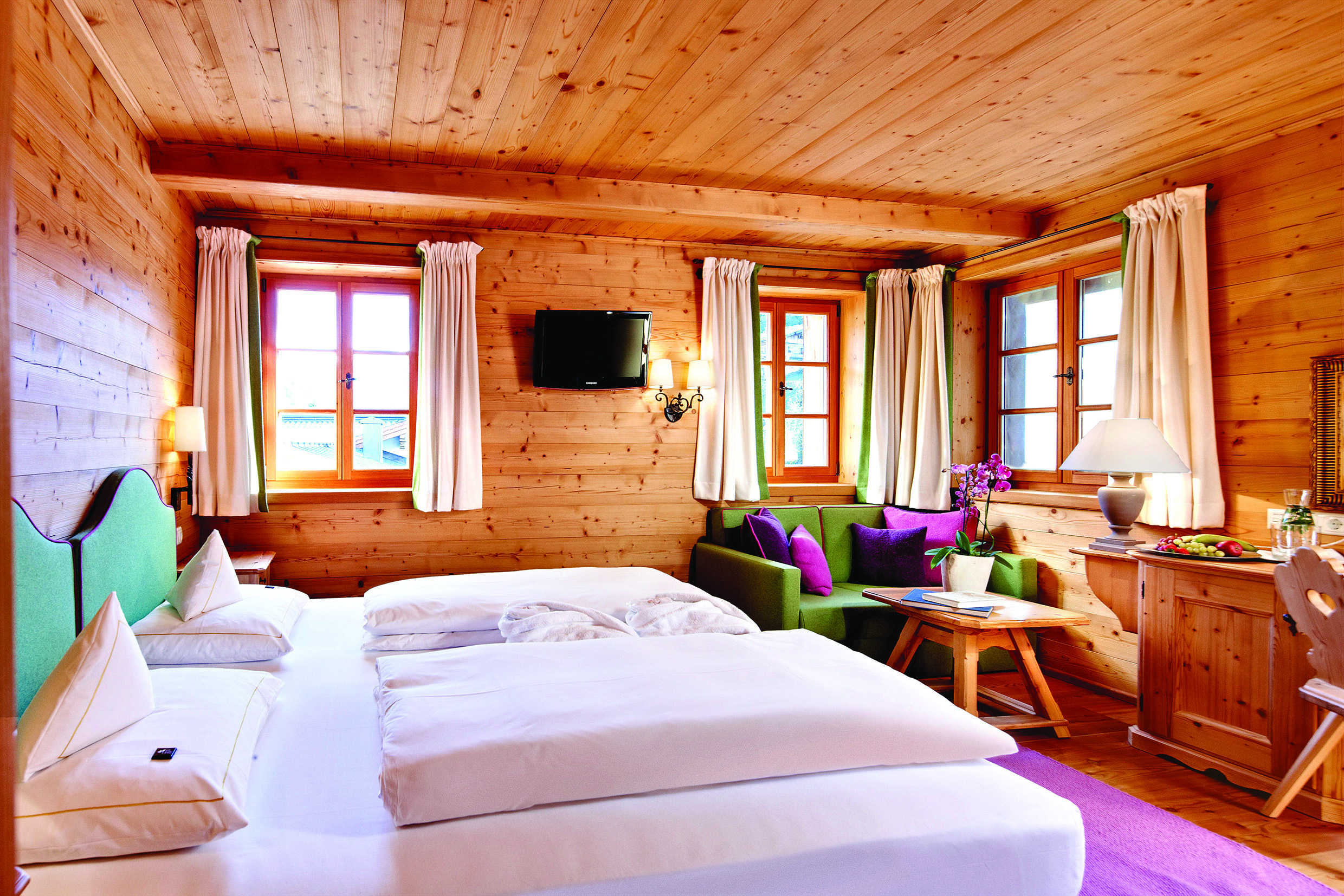 Standard room with wood pannelled ceiling, walls and floors with double bed and small windows
