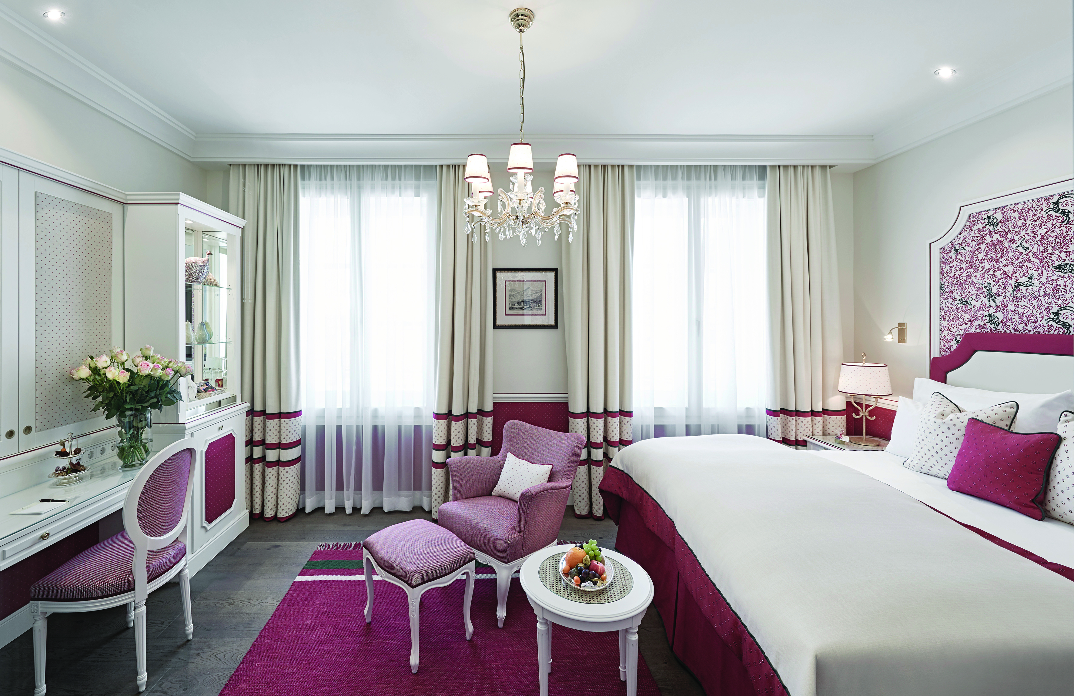 Hotel Sacher deluxe room, bed with pink and red details, vanity table, pink armchair