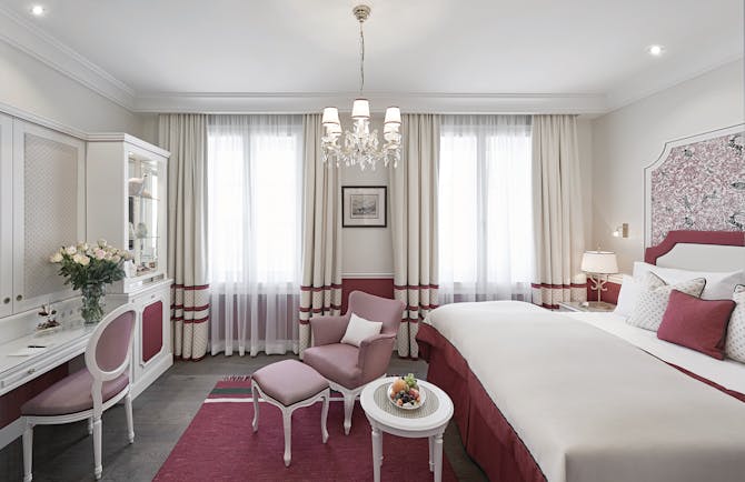 Hotel Sacher deluxe room, bed with pink and red details, vanity table, pink armchair