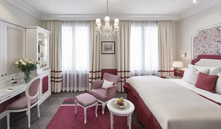 Hotel Sacher deluxe room, bed with pink and red details, vanity table, pink armchair