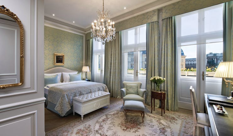 Hotel Sacher Vienna deluxe bedroom ornate mirror chandelier armchair with footstool and large windows