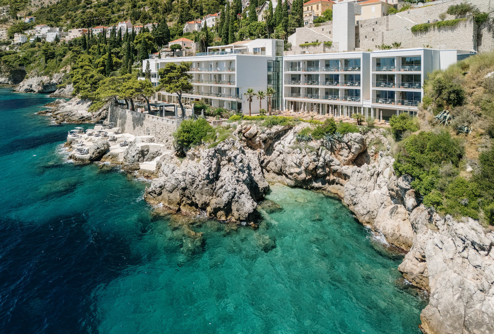 Villa Dubrovnik exterior, with white building lined with balconies looking out from the rocky coastline across the clear turquoise sea