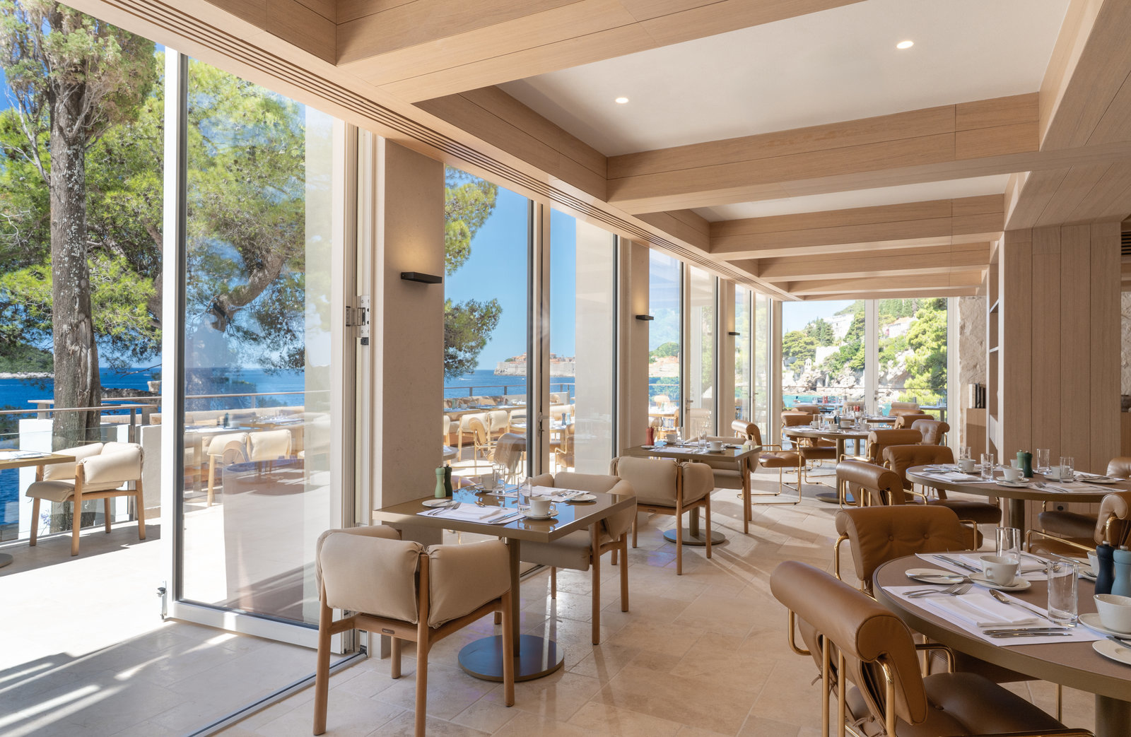 Villa Dubrovnik Pjerin restaurant interior with neutral palette, floor-to-ceiling windows, and views across the terrace and sea